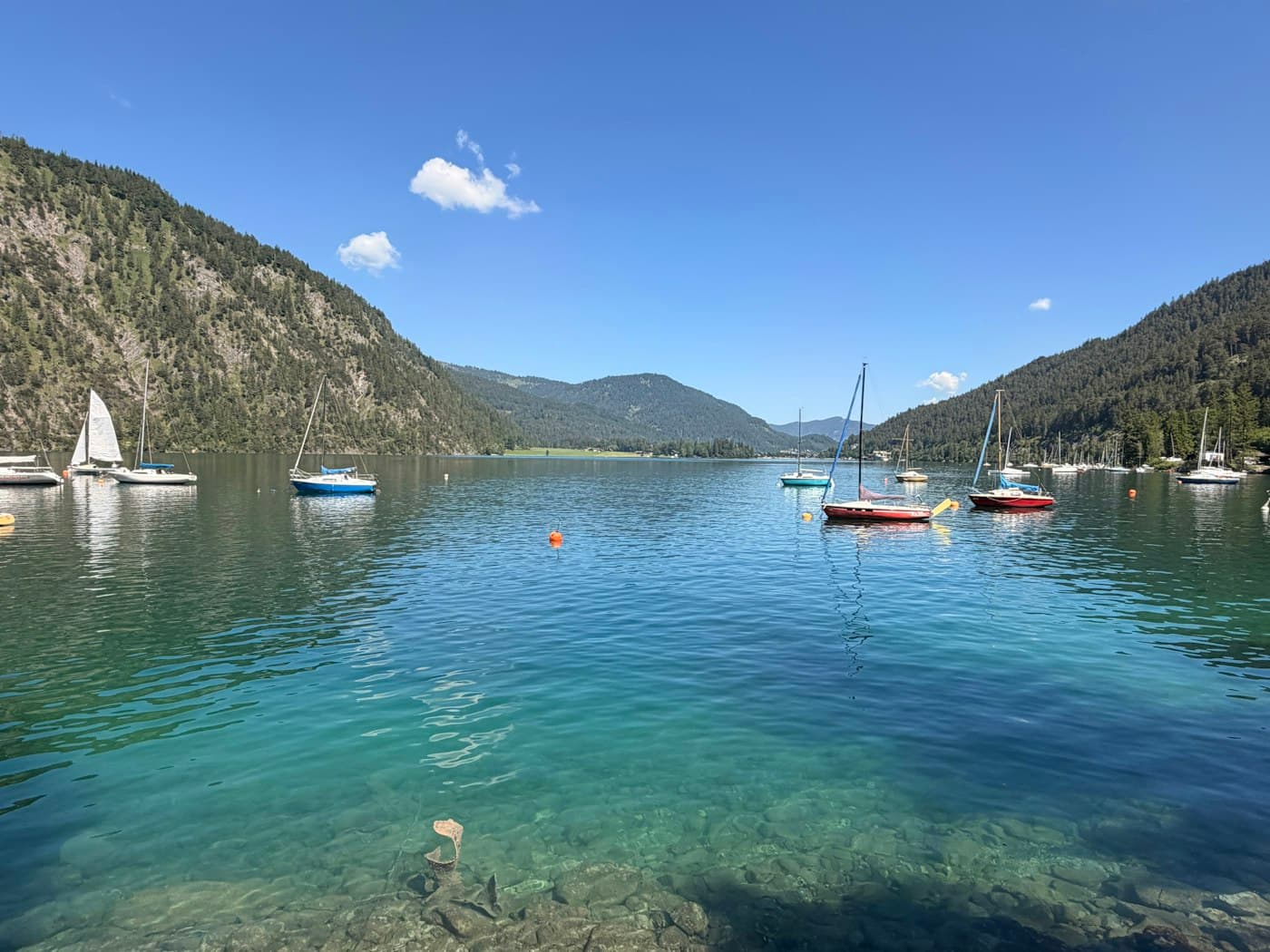 Sailboats moored on the clear green water of the Achensee, between wooded mountains