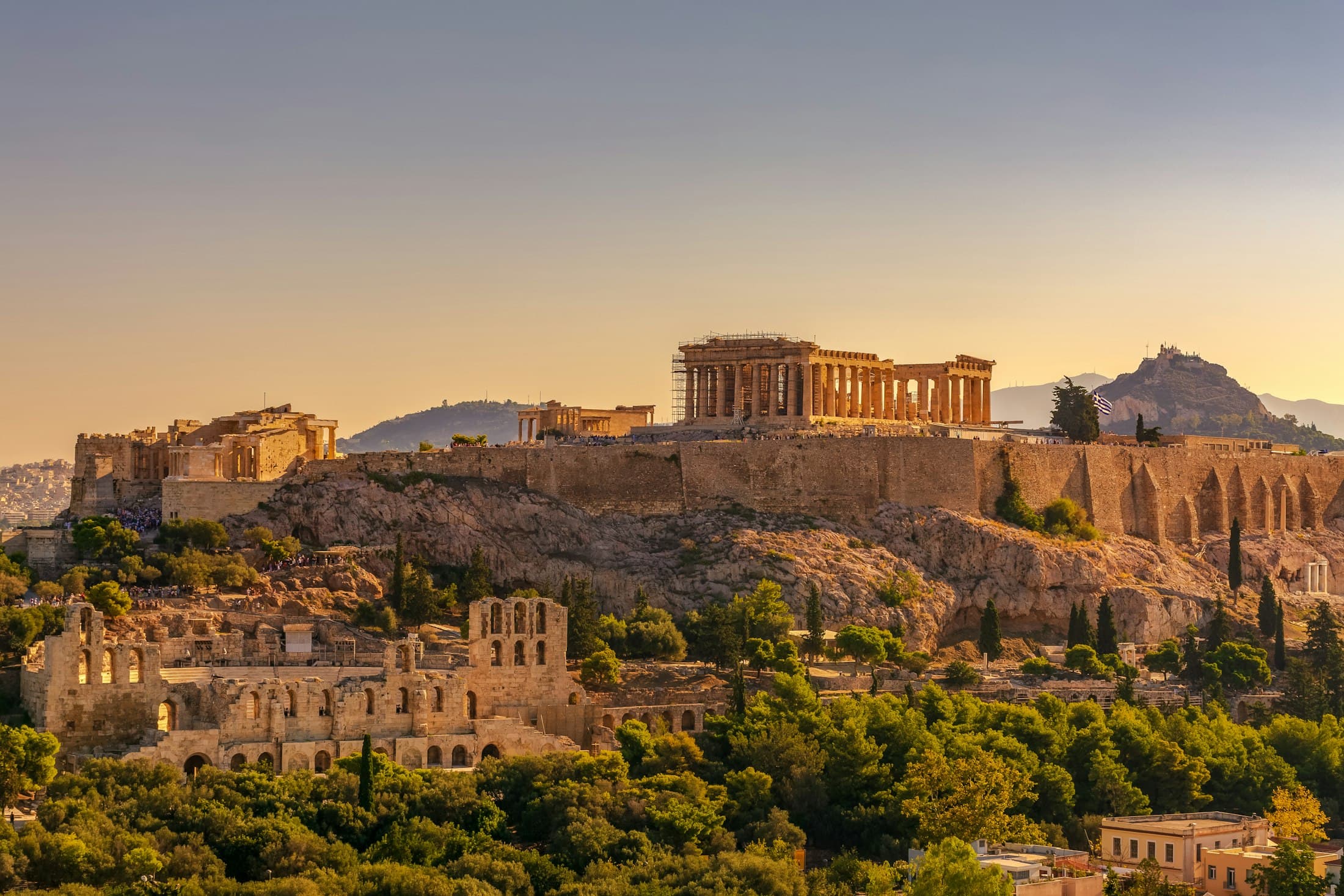 Der Parthenon und die Mauern der Akropolis im goldenen Abendlicht, darunter das Odeon des Herodes Atticus, dahinter der Lykabettus