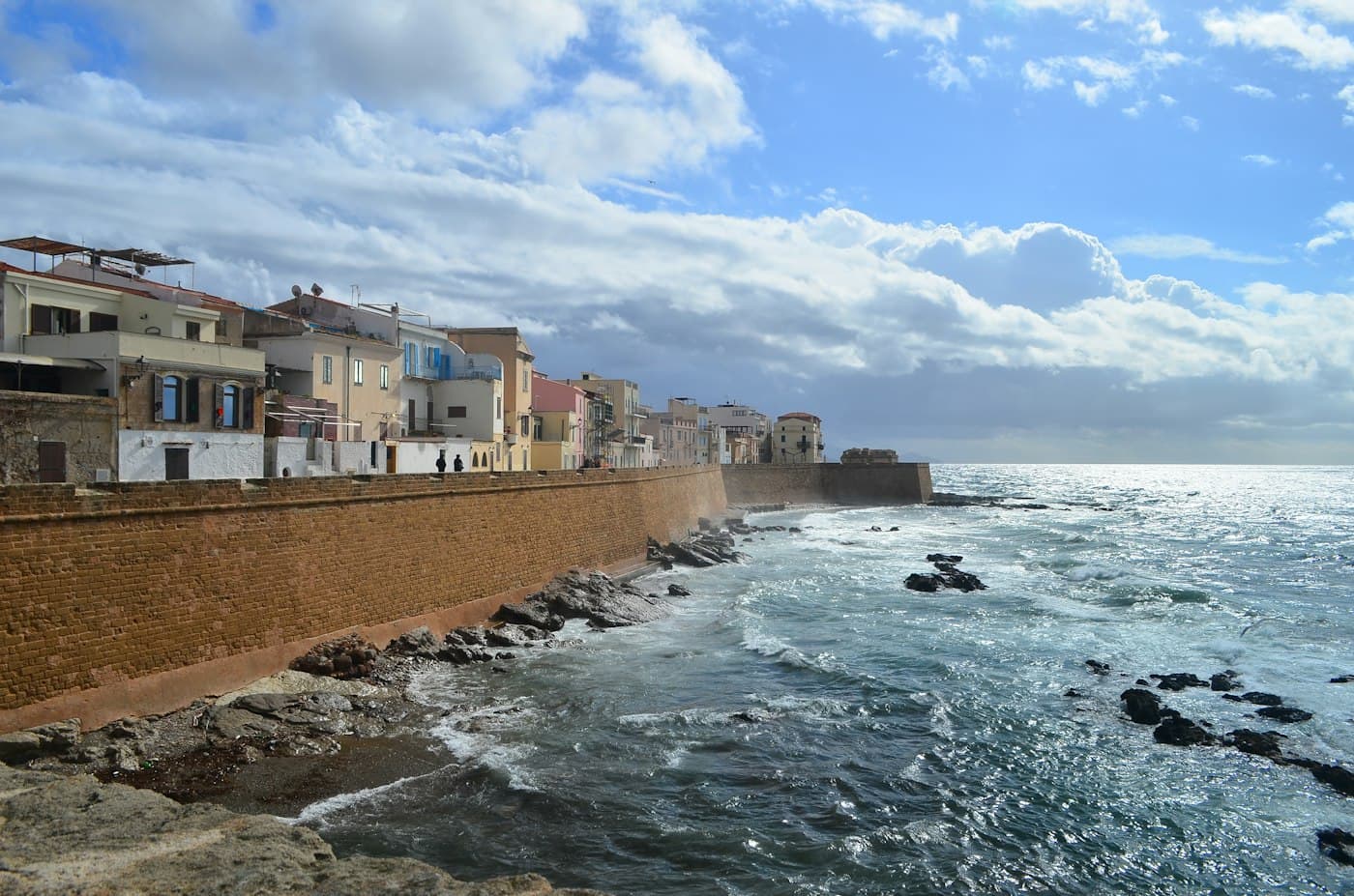 Häuser auf der alten Stadtmauer von Alghero über dem Meer, unten brechen sich die Wellen