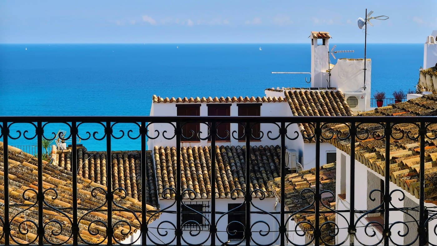 A wrought-iron balcony over tiled roofs and the blue sea in Altea
