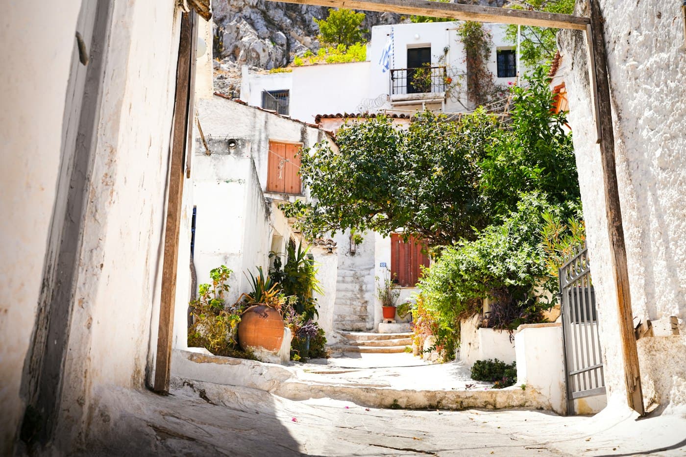 Eine weiß getünchte Gasse mit Topfpflanzen und einem Baum in Anafiotika, am Fuß des Akropolisfelsens