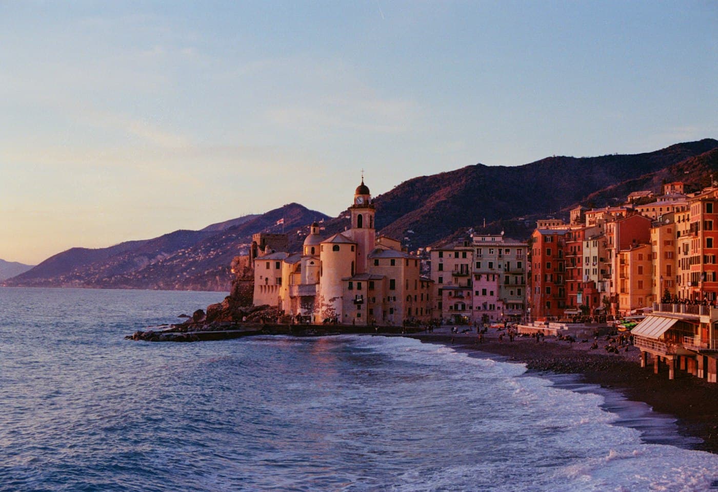 L’église de Camogli sur la pointe et ses hautes maisons colorées le long de la plage, au coucher du soleil