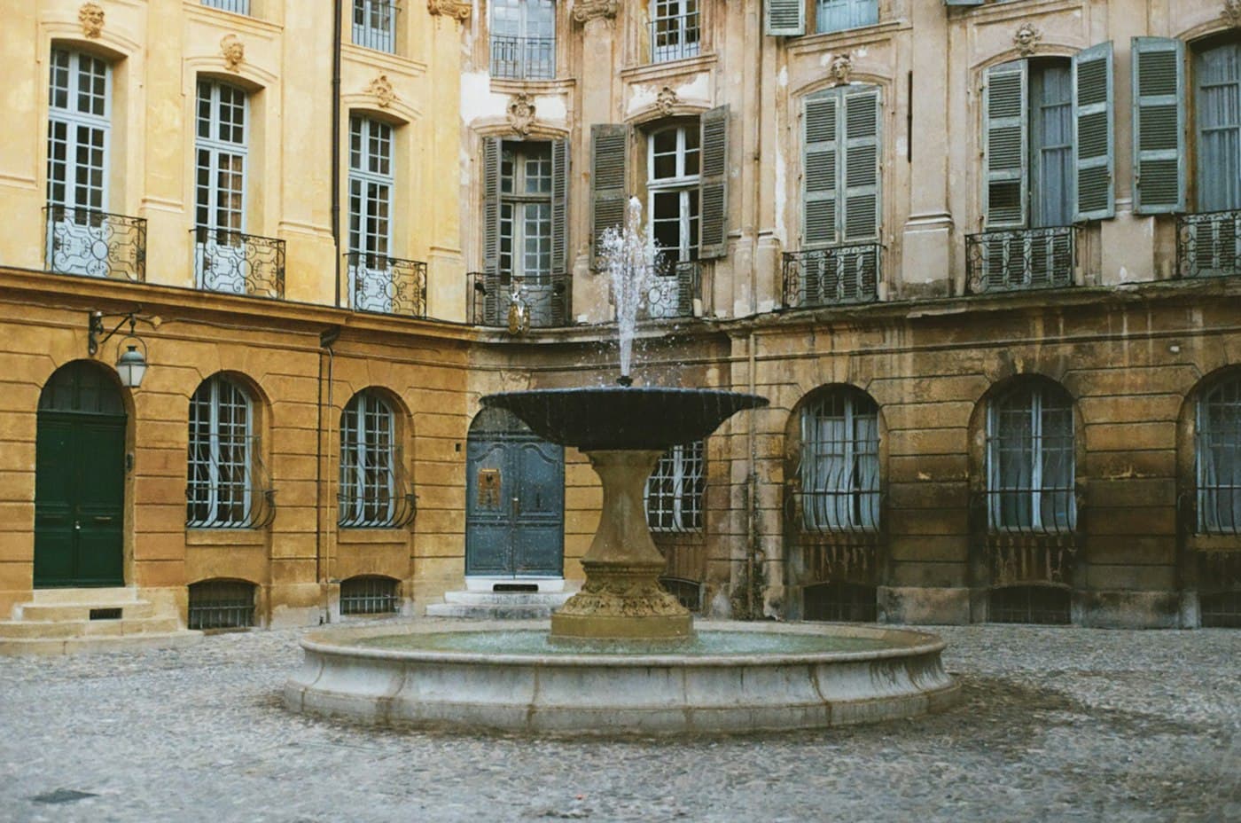 The fountain in the cobbled Place d’Albertas in Aix-en-Provence, ringed by tall shuttered façades with wrought-iron balconies