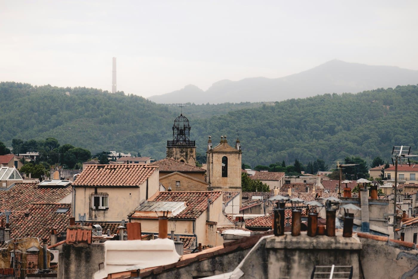 The tiled roofs and old bell towers of Aix-en-Provence, wooded hills behind under a soft grey sky