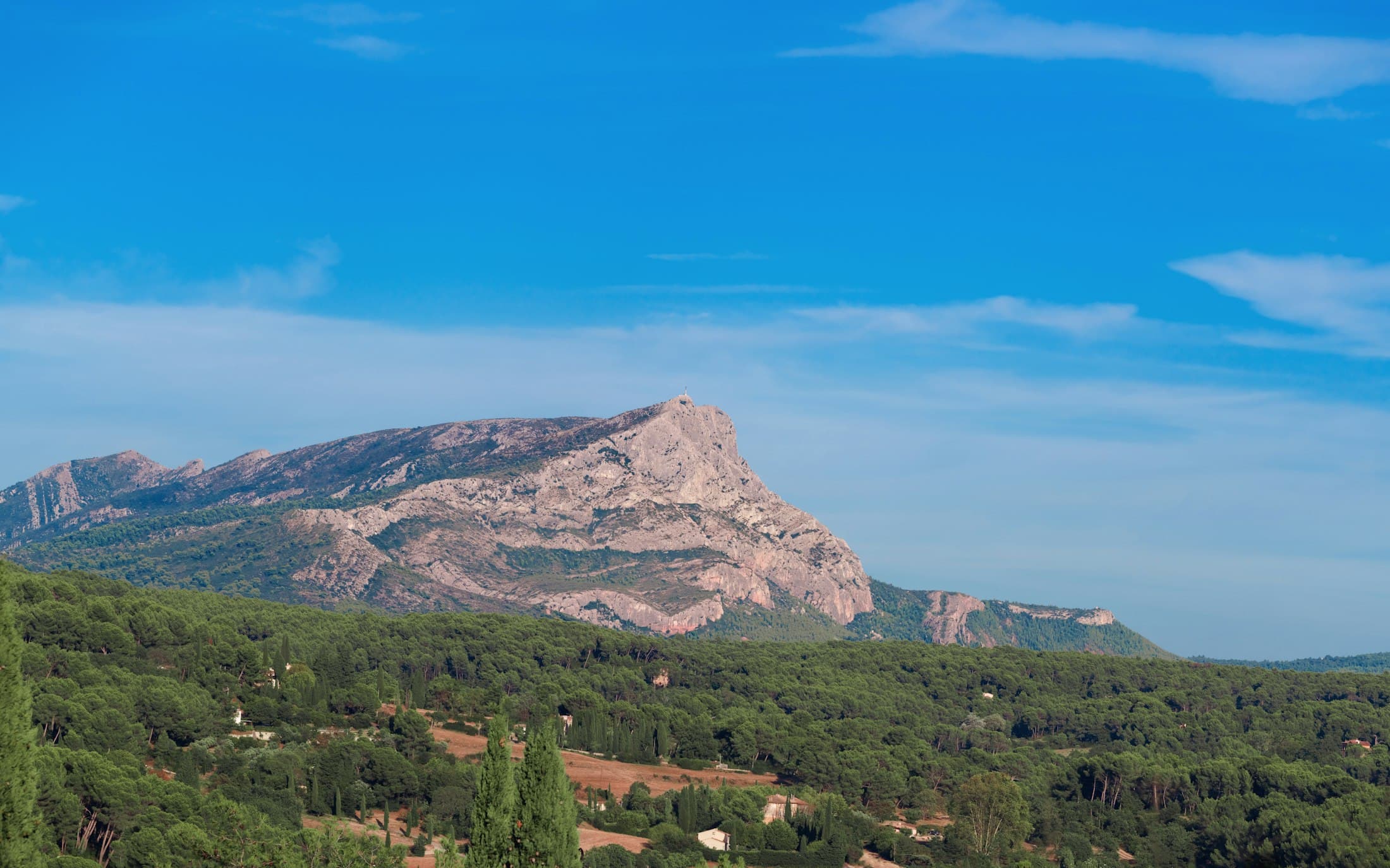 The Montagne Sainte-Victoire east of Aix-en-Provence, its pale limestone cliffs and the cross on the summit above pine woods and cypresses
