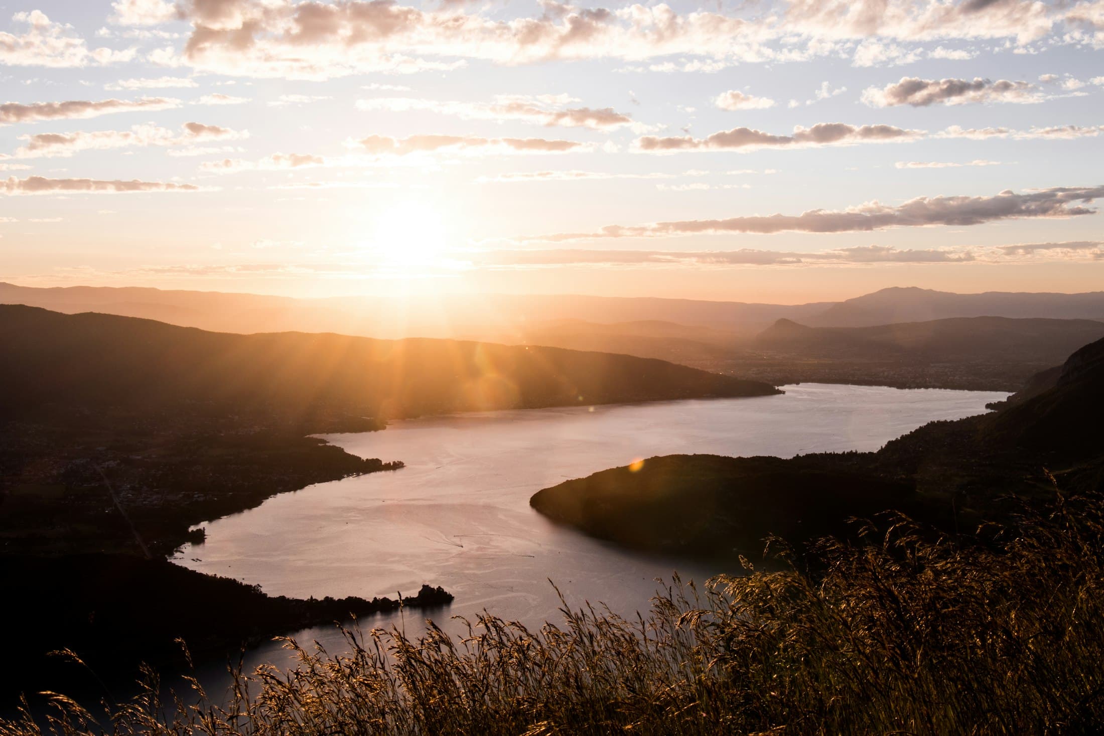 Sunset over Lake Annecy from the Col de la Forclaz, the lake narrowing between wooded hills, long grass in the foreground