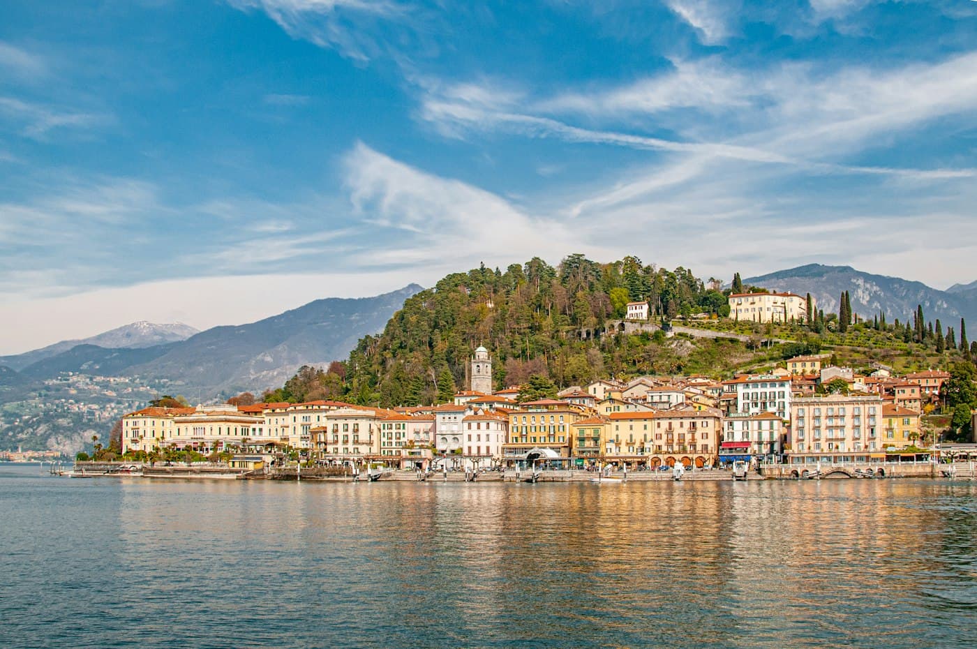 Bellagio’s lakefront houses and church tower seen from the water, the wooded hill above them
