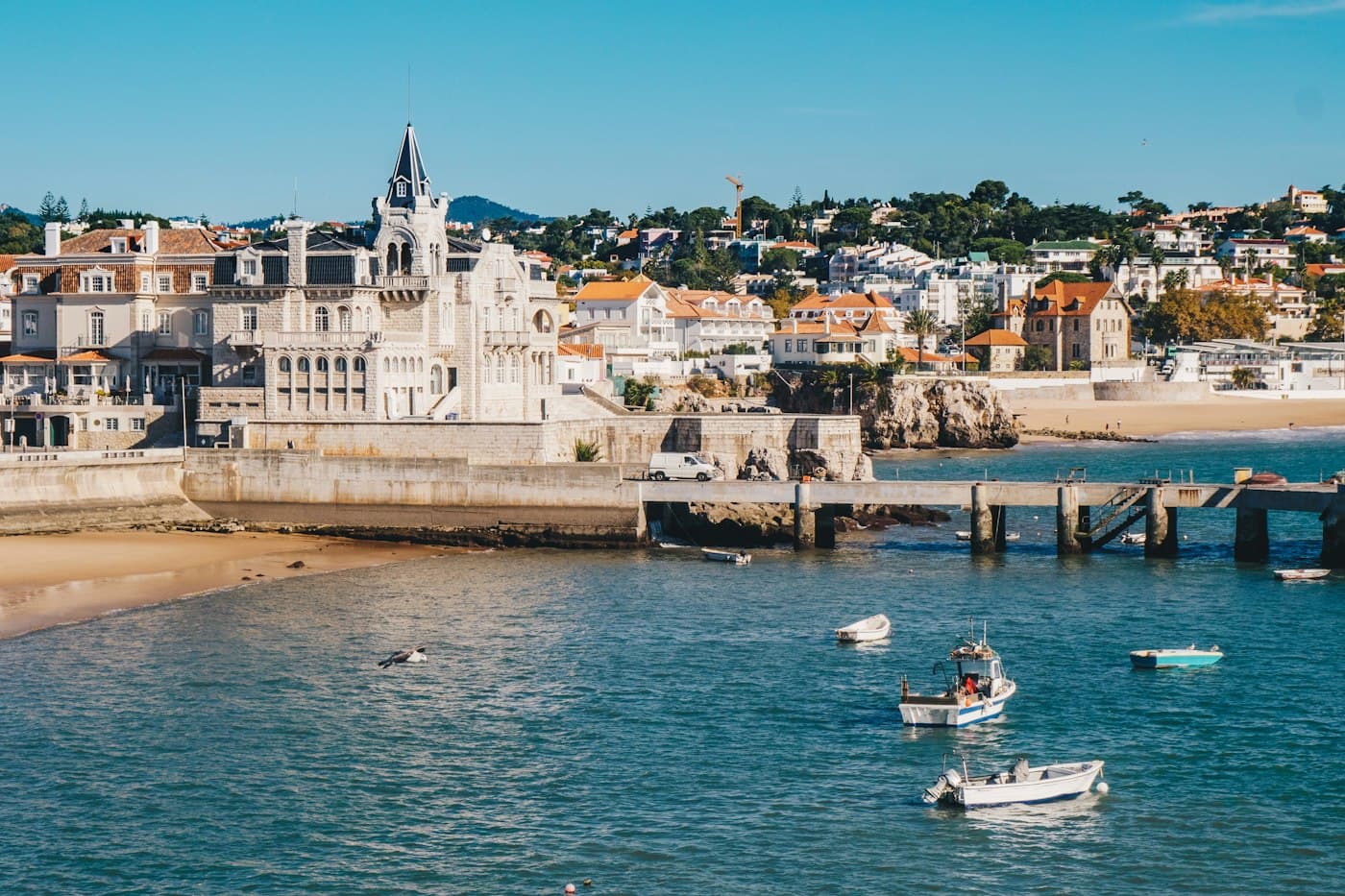 Pequenos barcos de pesca na baía de Cascais, um pontão e as casas brancas da marginal ao fundo
