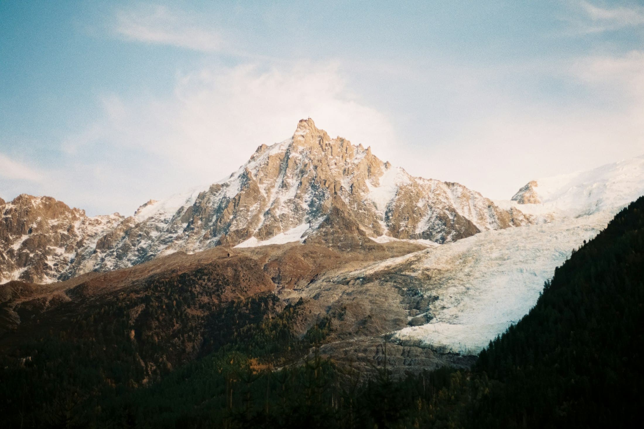 The Aiguille du Midi and the Bossons glacier above the Chamonix valley, warm light on the rock and dark forest below