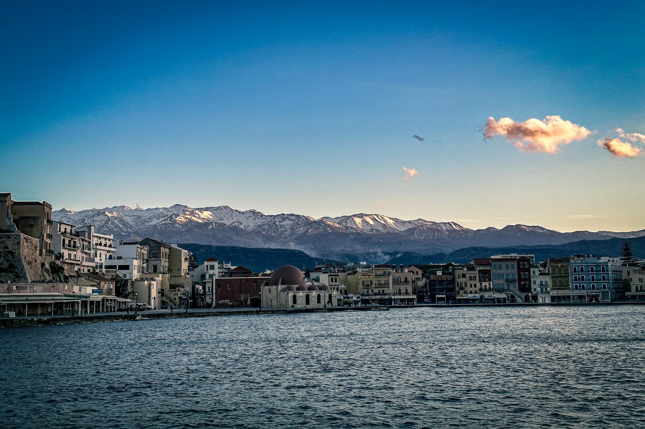 Chania’s Venetian harbour at dusk, the domed Küçük Hasan mosque on the waterfront and the snow-capped White Mountains behind