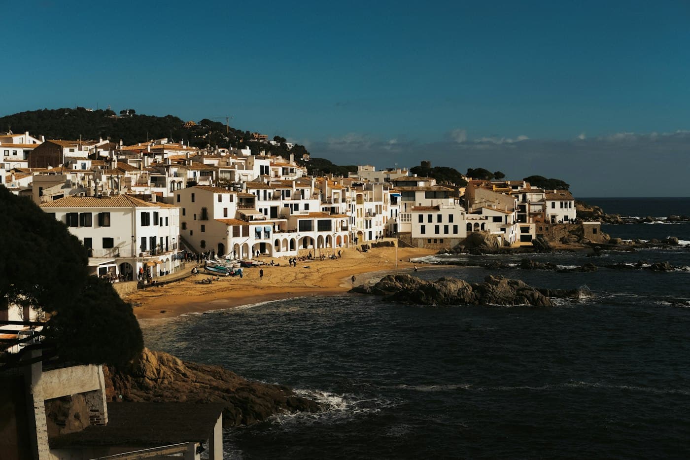 The white houses and arcades of Calella de Palafrugell along its beach, in low sunlight