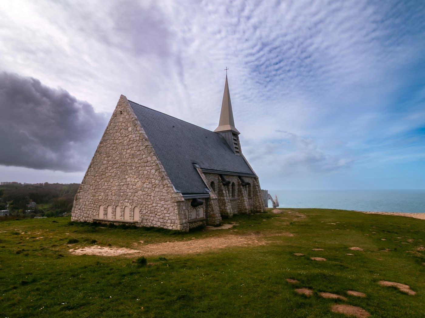 The stone chapel of Notre-Dame-de-la-Garde on the grassy top of the Falaise d’Amont, the arch and the Aiguille faint across the bay