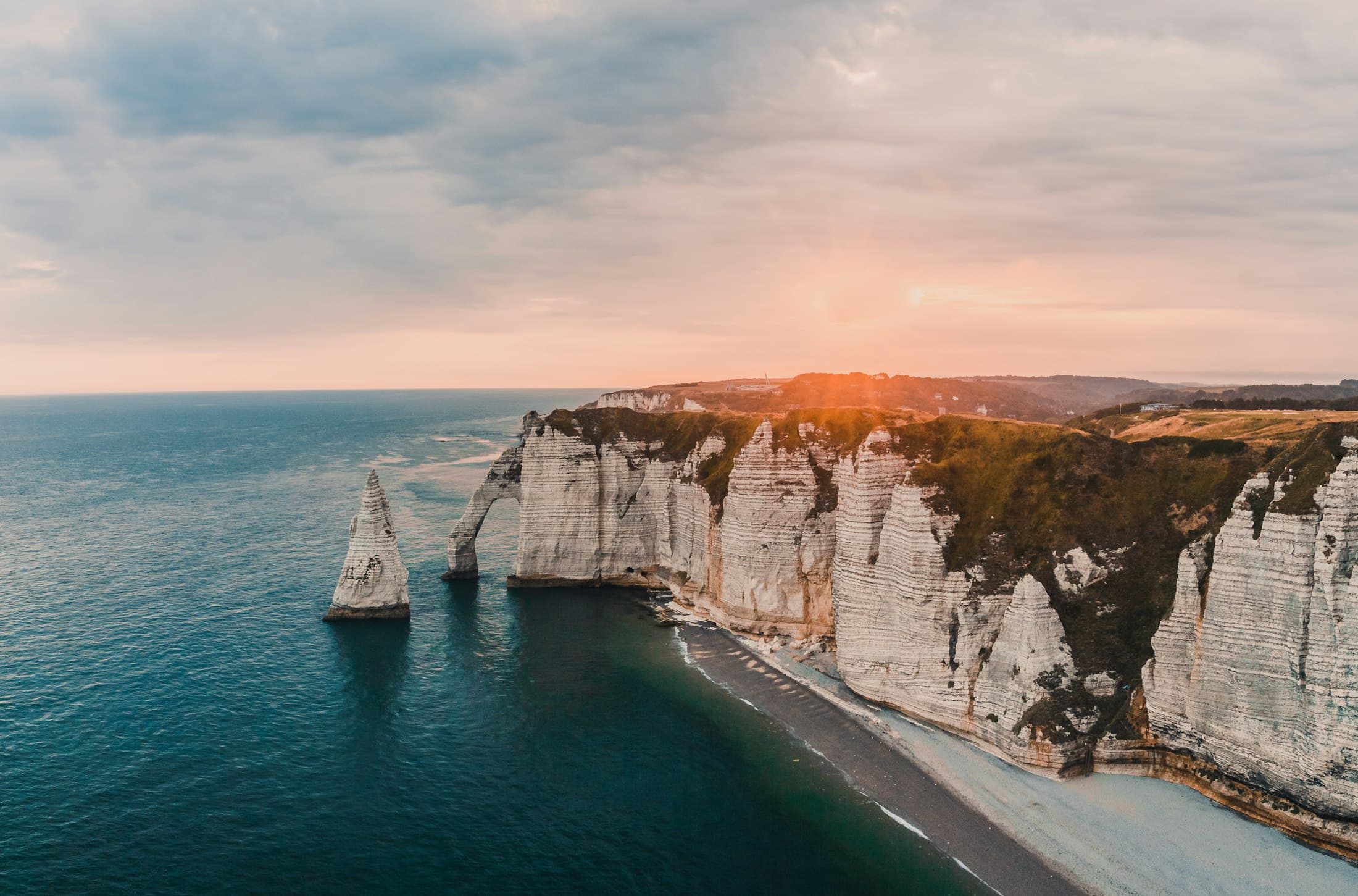 The Falaise d’Aval at Étretat from the air at sunset, its white chalk wall, the arch and the Aiguille standing in the sea, a pebble beach below