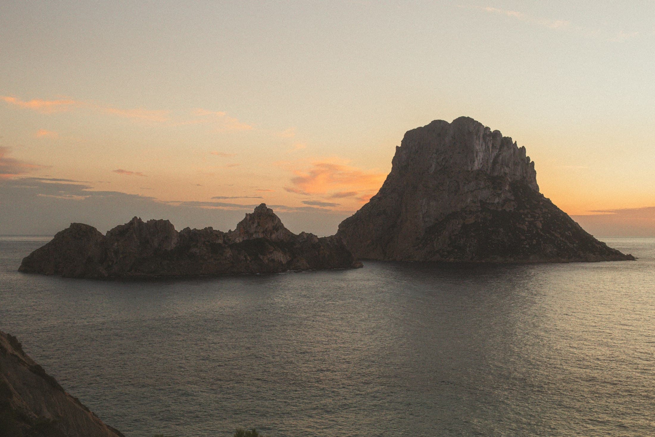 Es Vedrà y Es Vedranell frente a la costa de Ibiza al atardecer, oscuros contra un cielo naranja