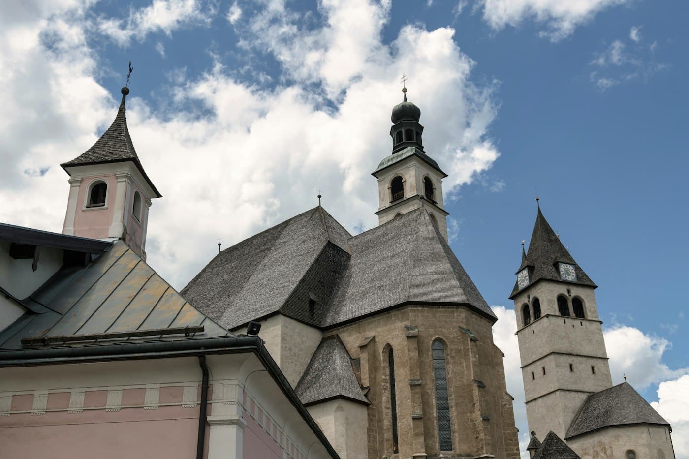 Kitzbühel’s parish church of St. Andreas and the tower of the Liebfrauenkirche beside it under a summer sky