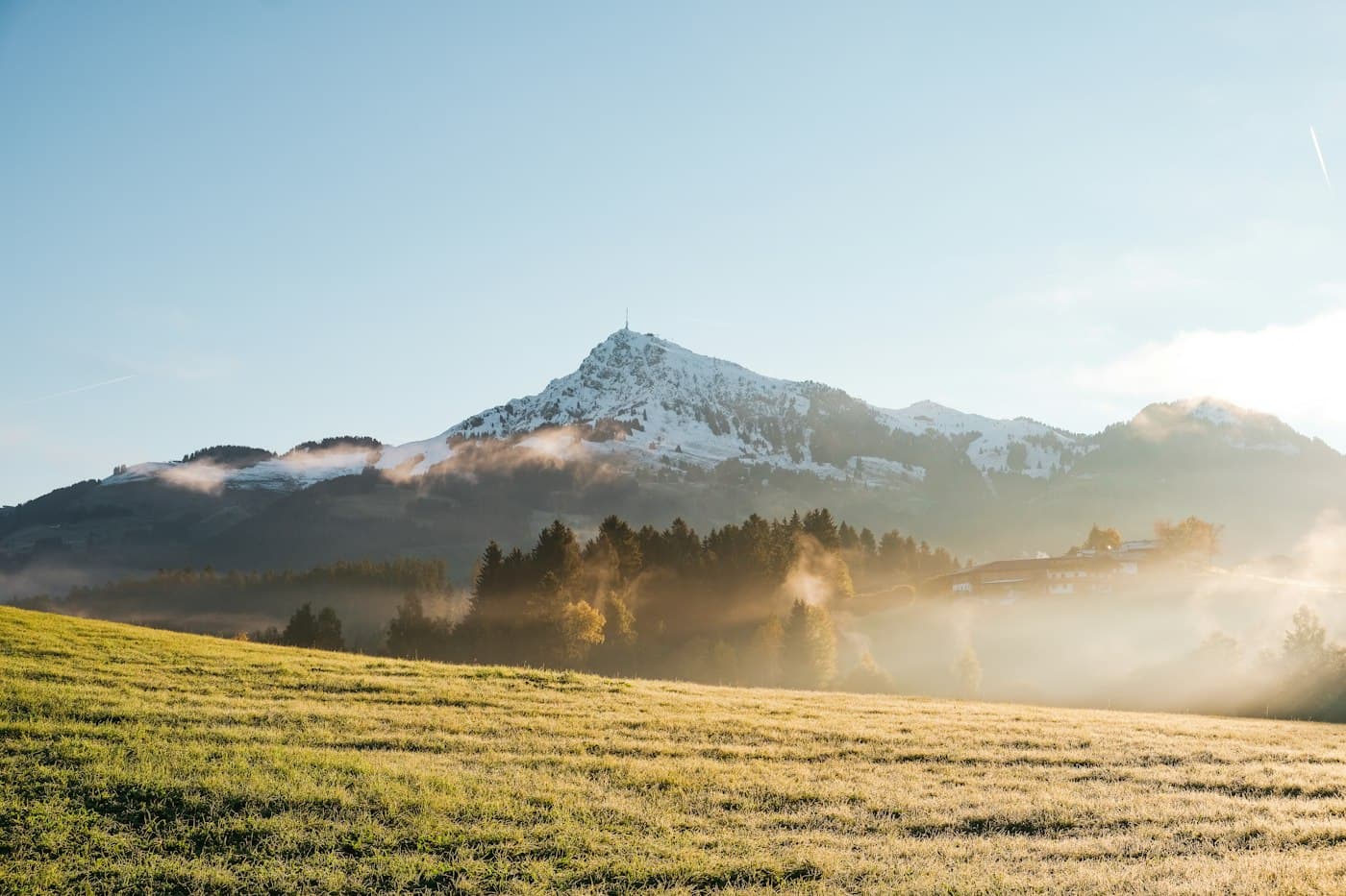 The Kitzbüheler Horn dusted with early snow above frosty autumn meadows, morning mist rising from the woods