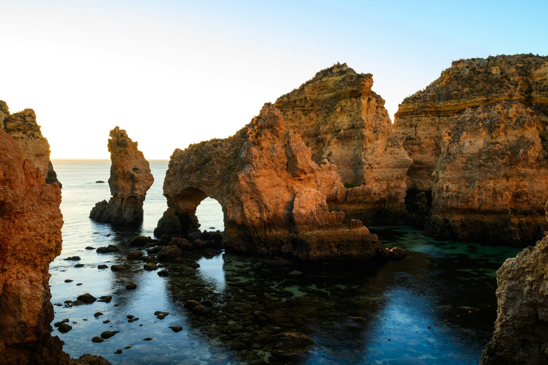Sea stacks and a rock arch at Ponta da Piedade, Lagos, lit gold by the early sun over still, clear water