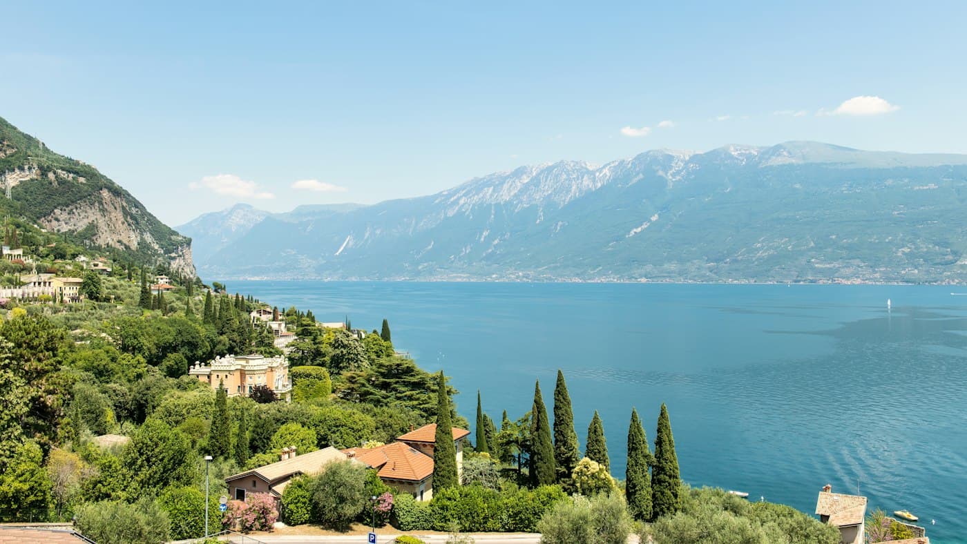 Ville e cipressi su un pendio verde sopra l’acqua azzurra del Lago di Garda, con i monti sull’altra sponda