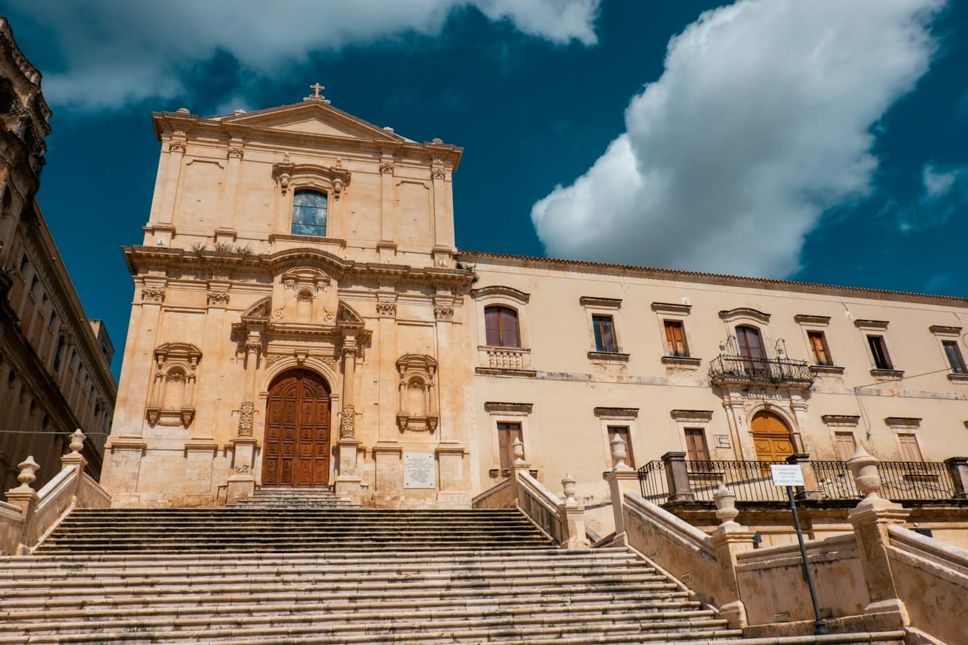 Una lunga scalinata di pietra che sale alla facciata barocca di una chiesa a Noto, sotto un cielo blu intenso
