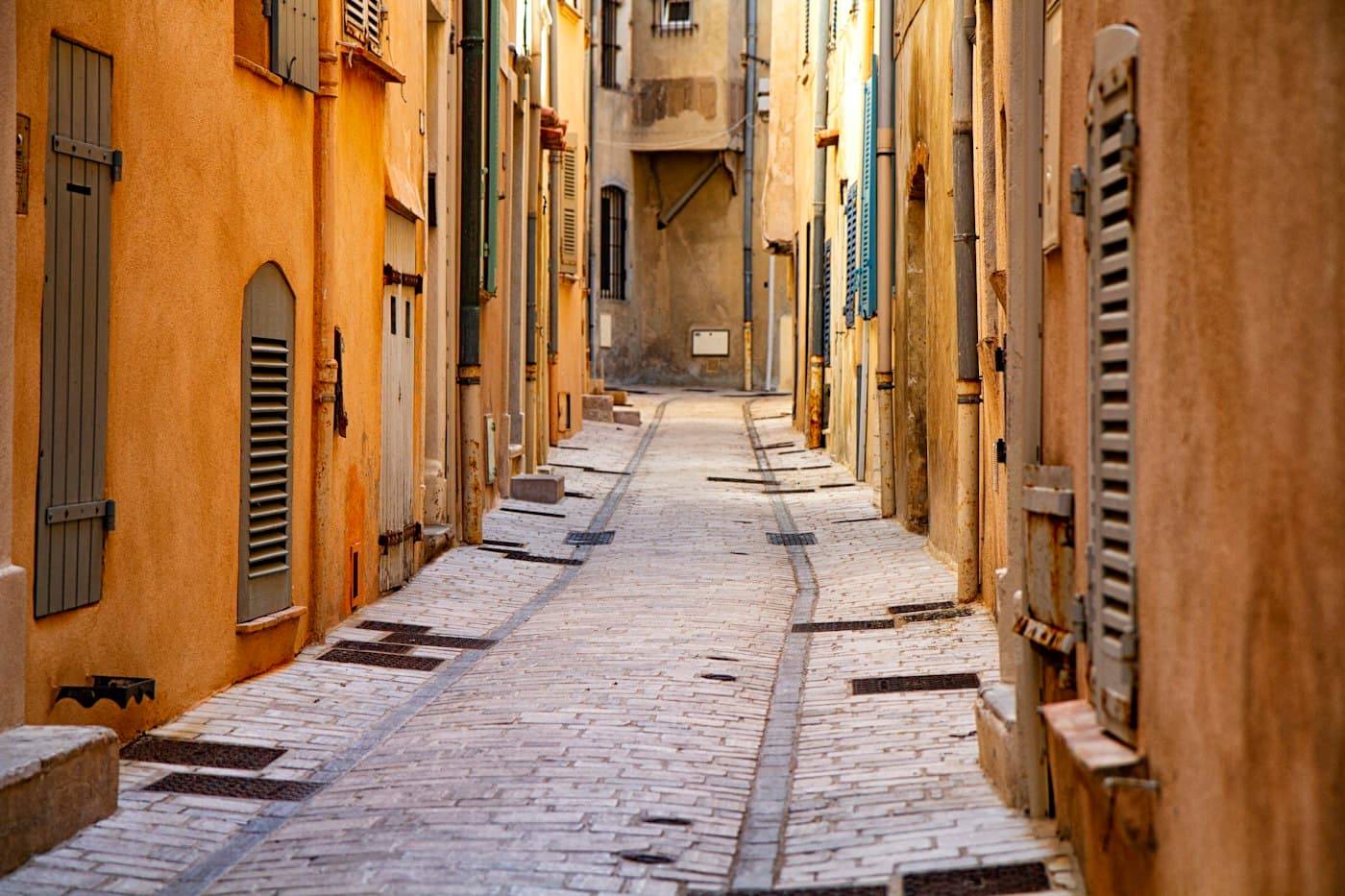 An empty lane in Saint-Tropez between ochre walls and grey and blue shutters, in warm side light