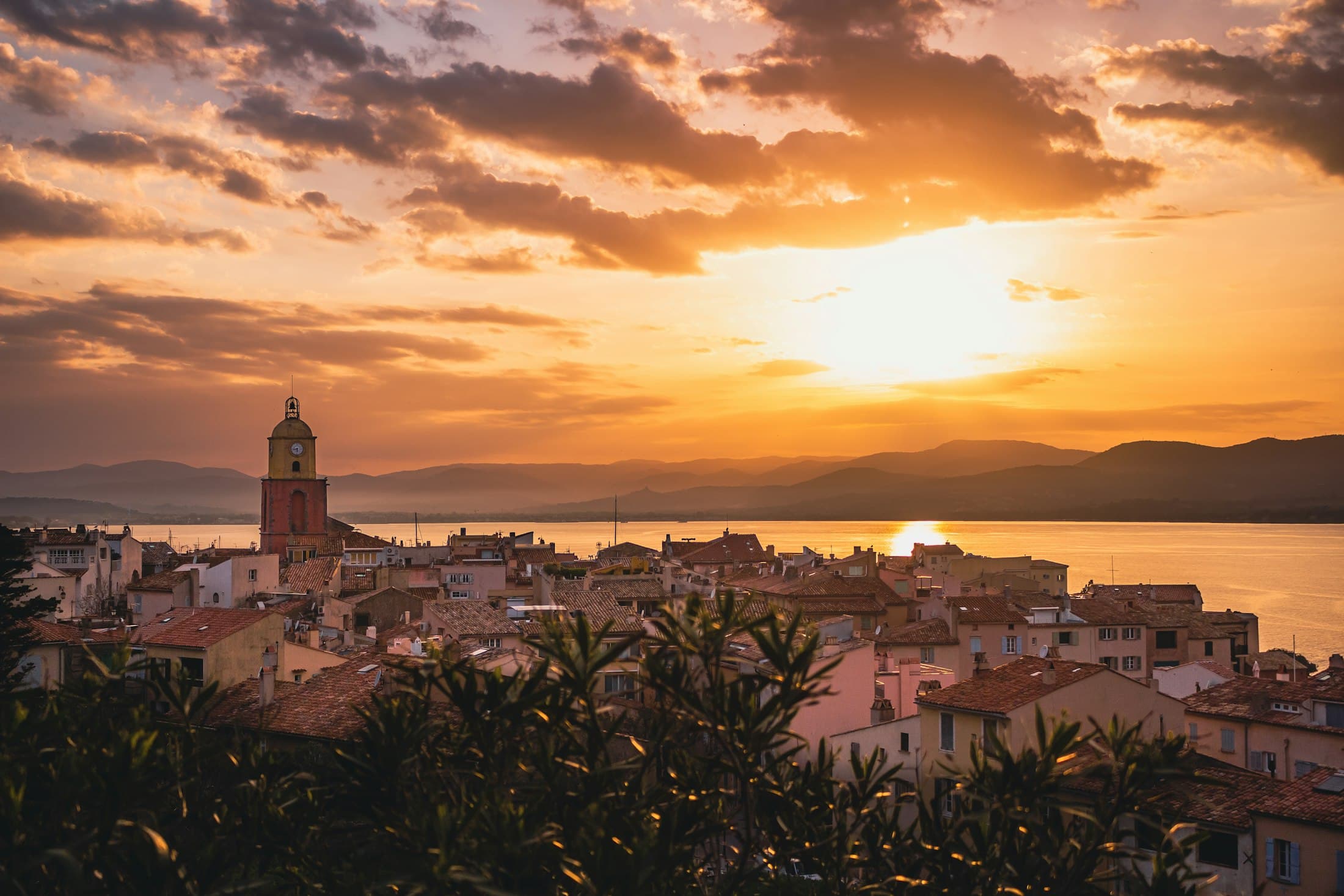 Saint-Tropez at sunset: the old town’s roofs and its bell tower against a golden sky, the gulf and the hills beyond