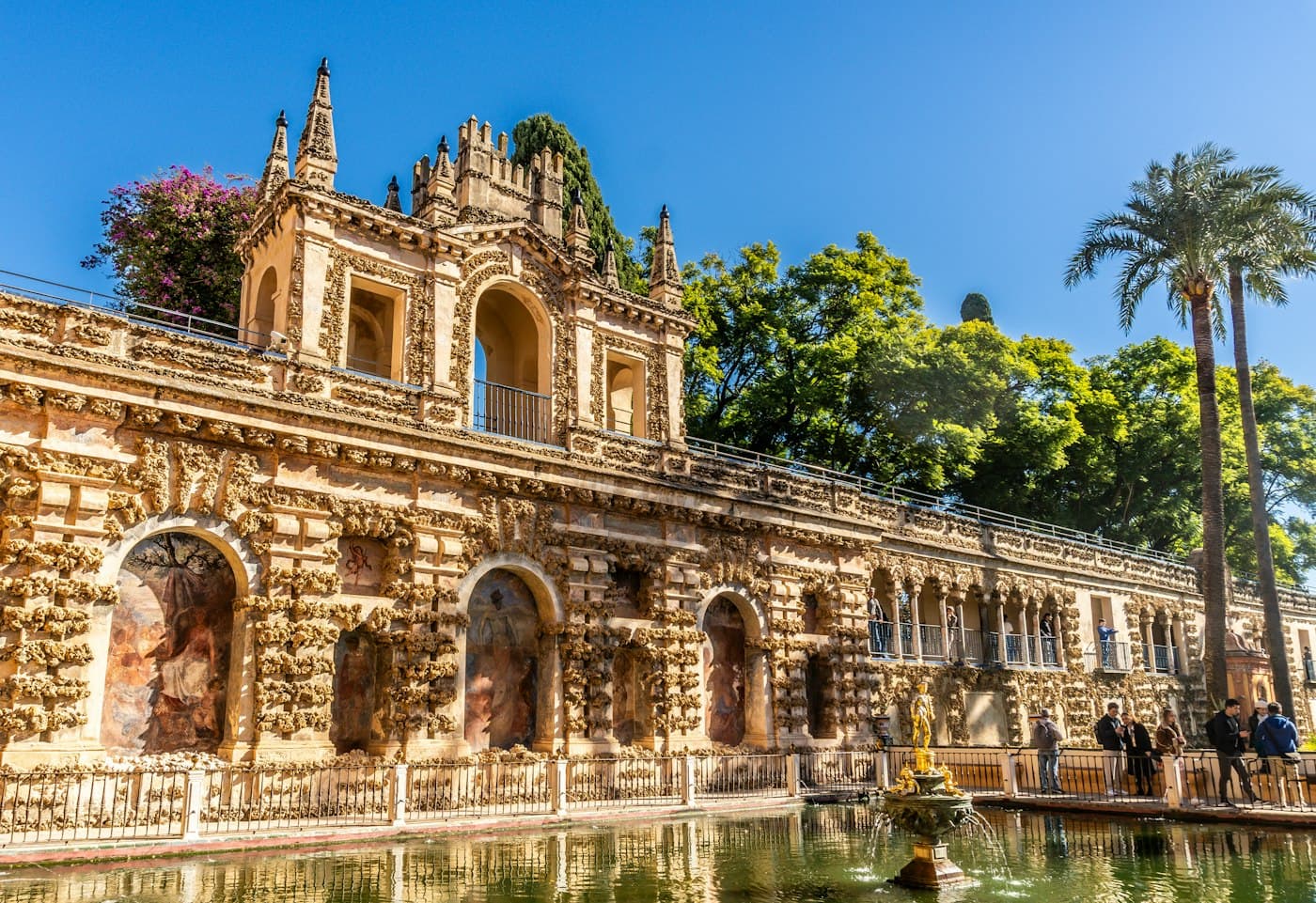 La galería del Grutesco sobre el estanque de Mercurio en los jardines del Real Alcázar de Sevilla, con palmeras y buganvillas detrás