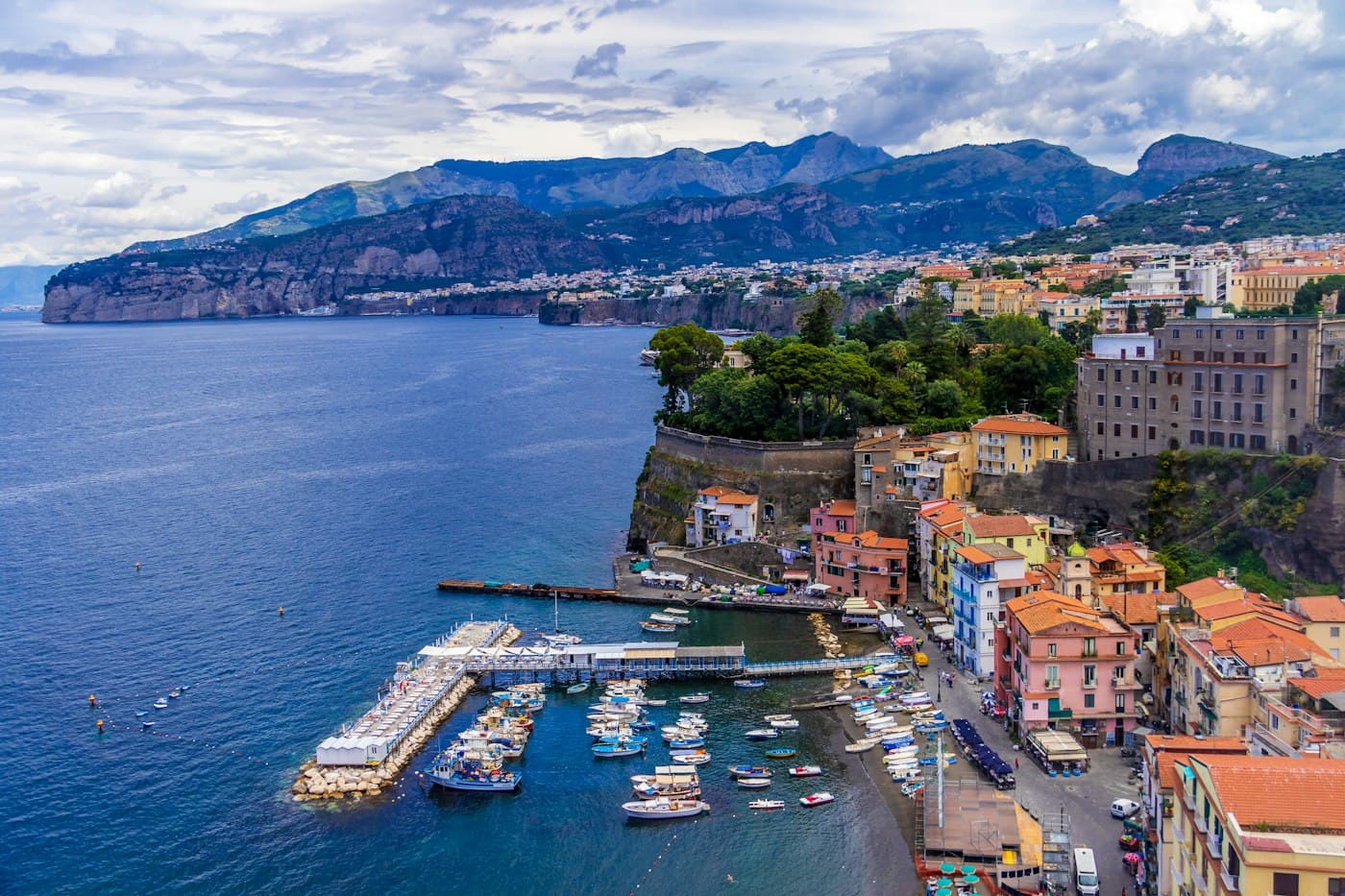 Marina Grande dall’alto: case color pastello ai piedi della falesia, una spiaggia piena di barche da pesca e un pontile di legno che entra nell’acqua blu