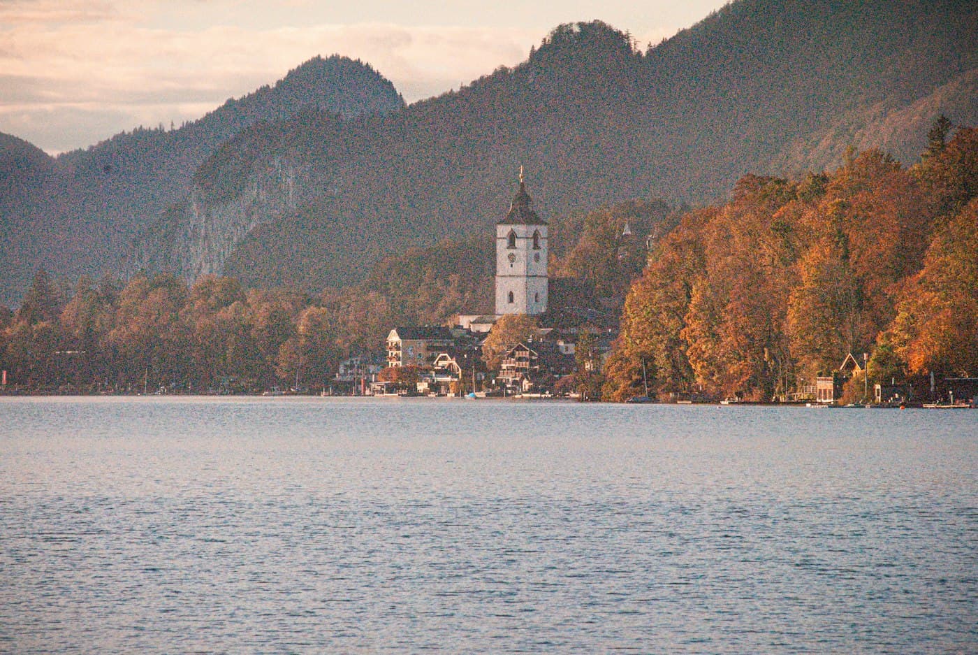 St. Wolfgang across the lake on an autumn evening, the church tower among the lakeside houses and the woods turning orange on the shore