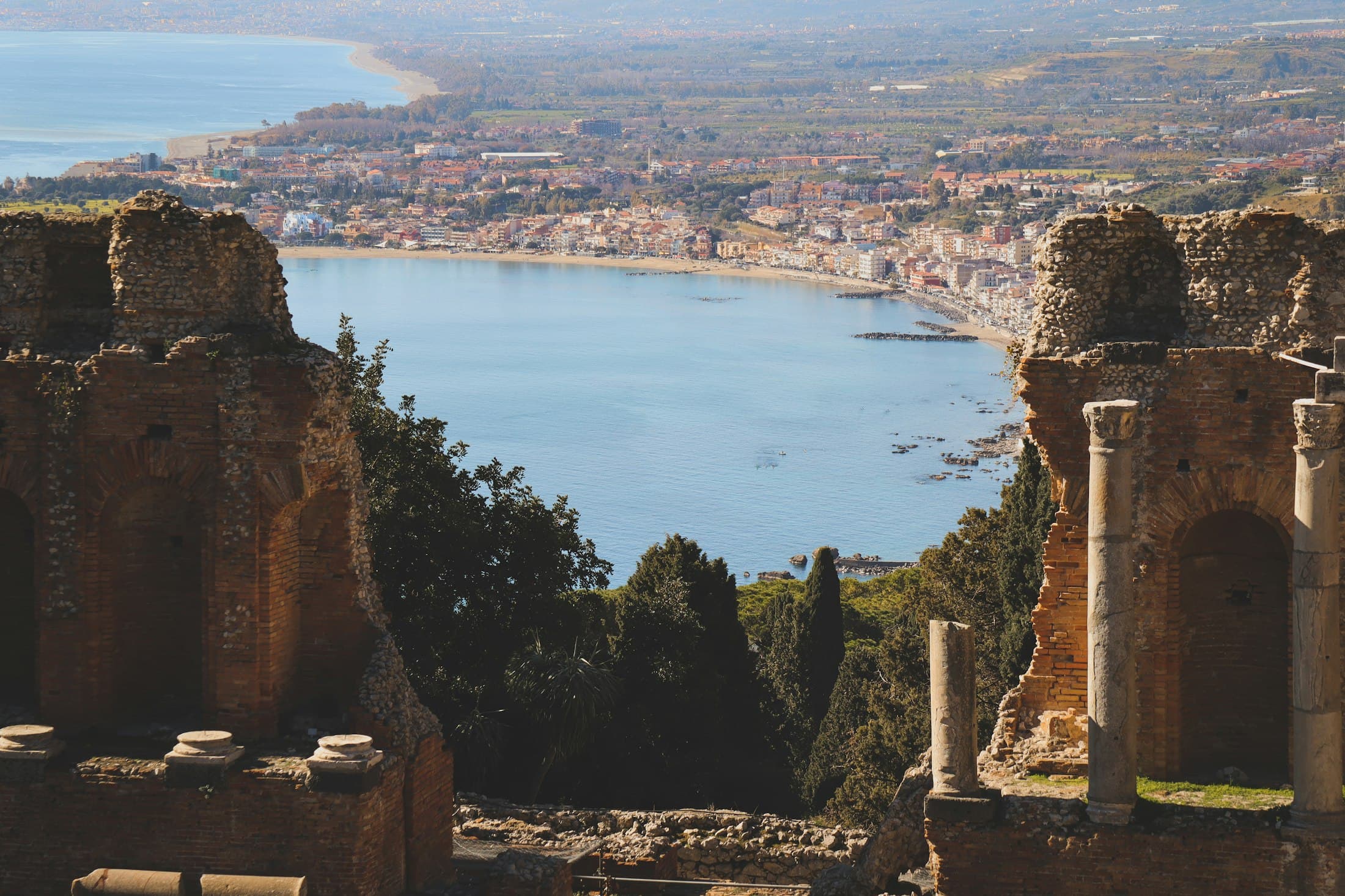La baia sotto Taormina incorniciata dalle rovine in mattoni del teatro antico