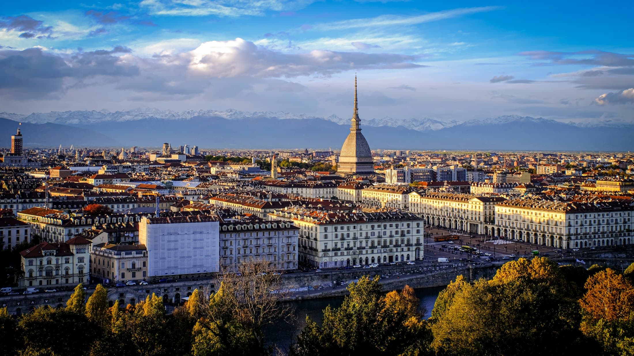 La Mole Antonelliana sopra i tetti di Torino e i portici di piazza Vittorio Veneto nel sole basso d’autunno, con le Alpi innevate alle spalle