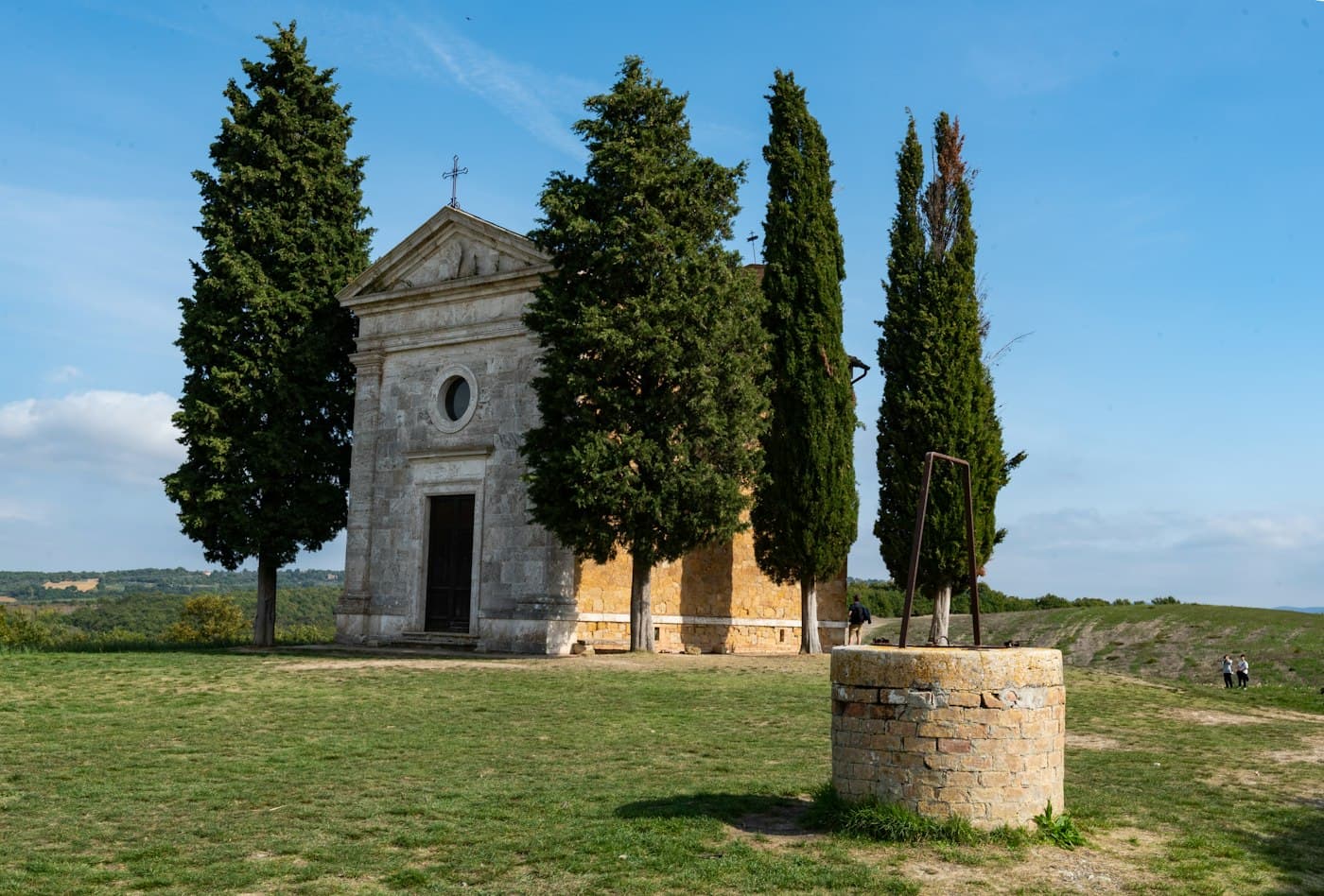 The small stone chapel of the Madonna di Vitaleta among cypresses, an old well on the lawn in front