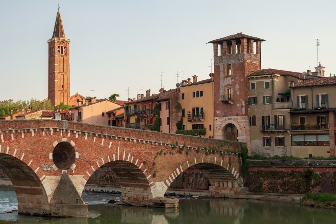 Ponte Pietra nella luce calda della sera, le arcate di mattoni e pietra sull’Adige verde, un alto campanile di mattoni e vecchie case alle spalle