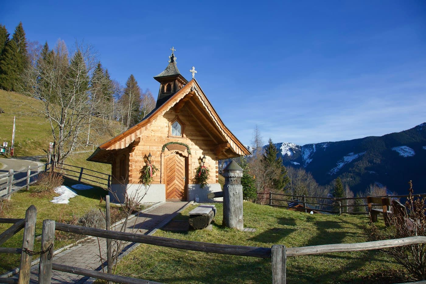 A small wooden chapel with a shingled bell turret on a hillside at Zell am See, a fenced path leading to its carved door