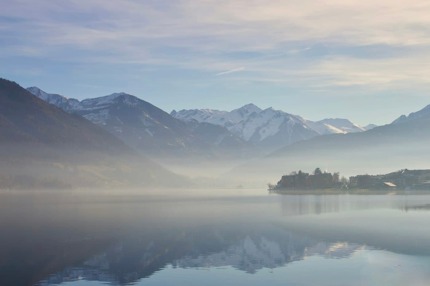 Morning mist on the Zeller See, the snow-capped mountains to the south mirrored in the still water