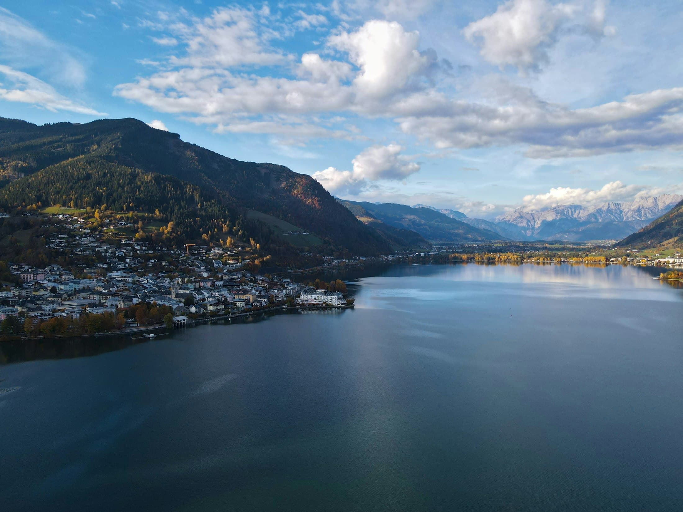 Zell am See aus der Luft an einem Herbstnachmittag: die Stadt am Westufer, der Zeller See zieht sich nach Süden zu verschneiten Gipfeln