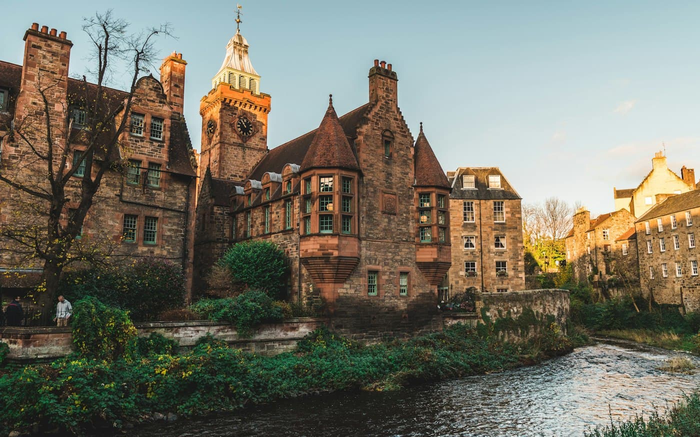 Dean Village con un sol bajo y dorado: la piedra roja, las torrecillas y la torre del reloj de Well Court sobre el Water of Leith