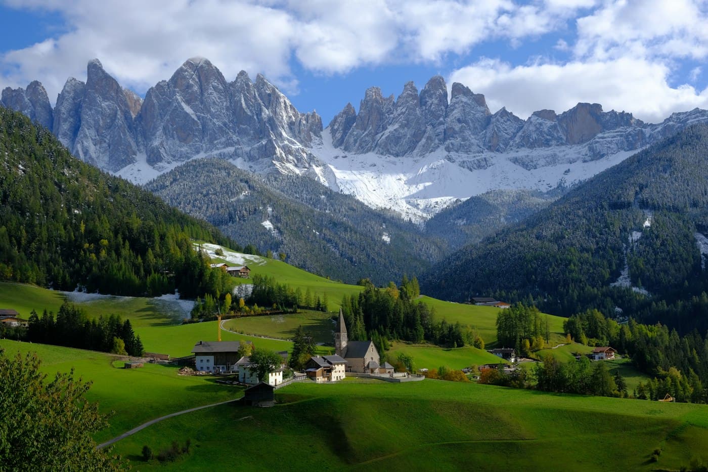 Uma igreja de aldeia entre prados verdes, aos pés das Odle, no Val di Funes