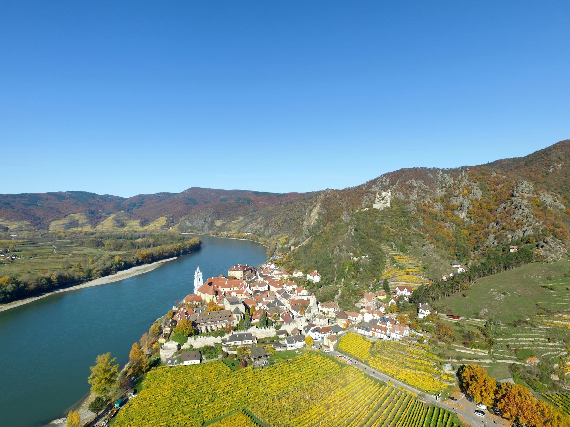 Der blaue Kirchturm und die Altstadt von Dürnstein an der Donau zwischen herbstlich goldenen Weingärten, darüber die Burgruine am Hang