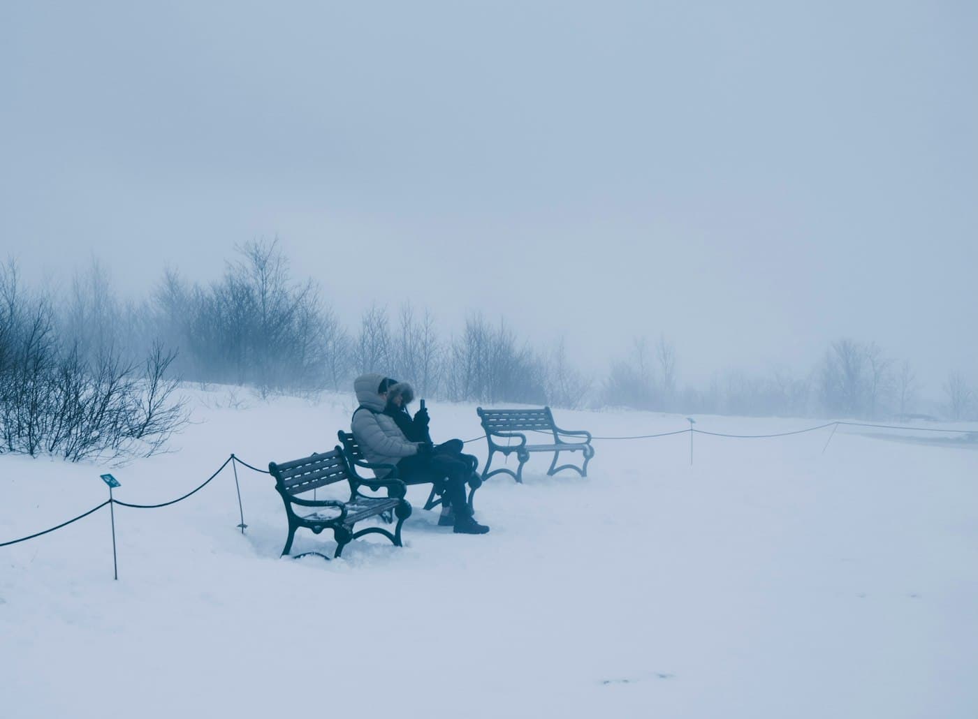 Ein warm eingepacktes Paar auf einer Bank in Schnee und Nebel am Geysir