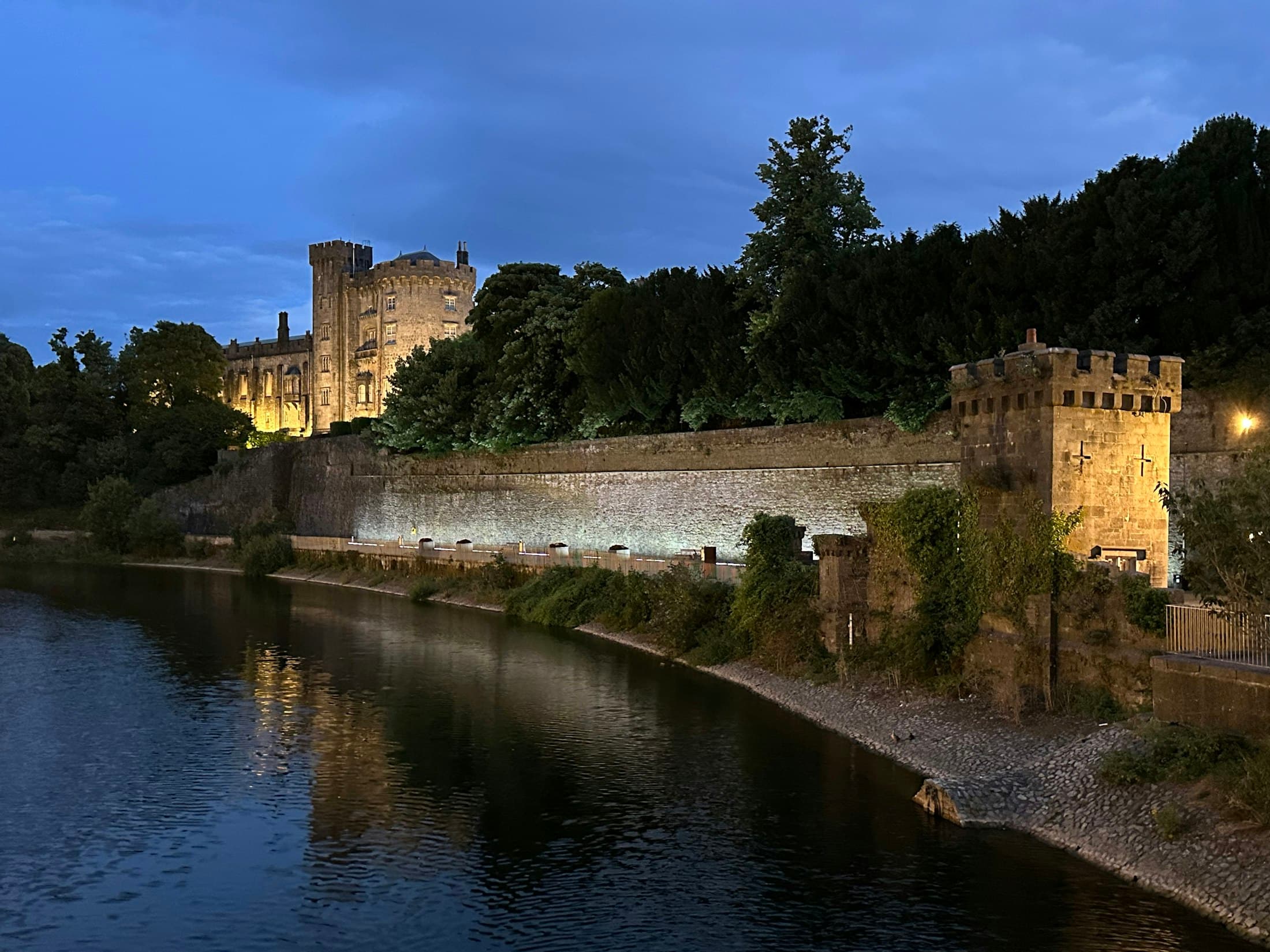 Il castello di Kilkenny illuminato al crepuscolo sopra le sue mura sul fiume, con il Nore davanti