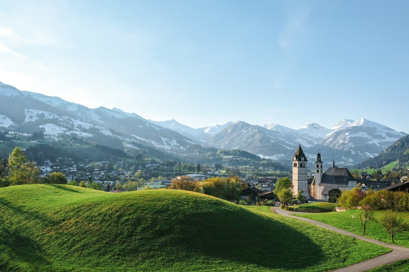 Kitzbühel’s church towers beyond green hillocks, the mountains behind still streaked with snow