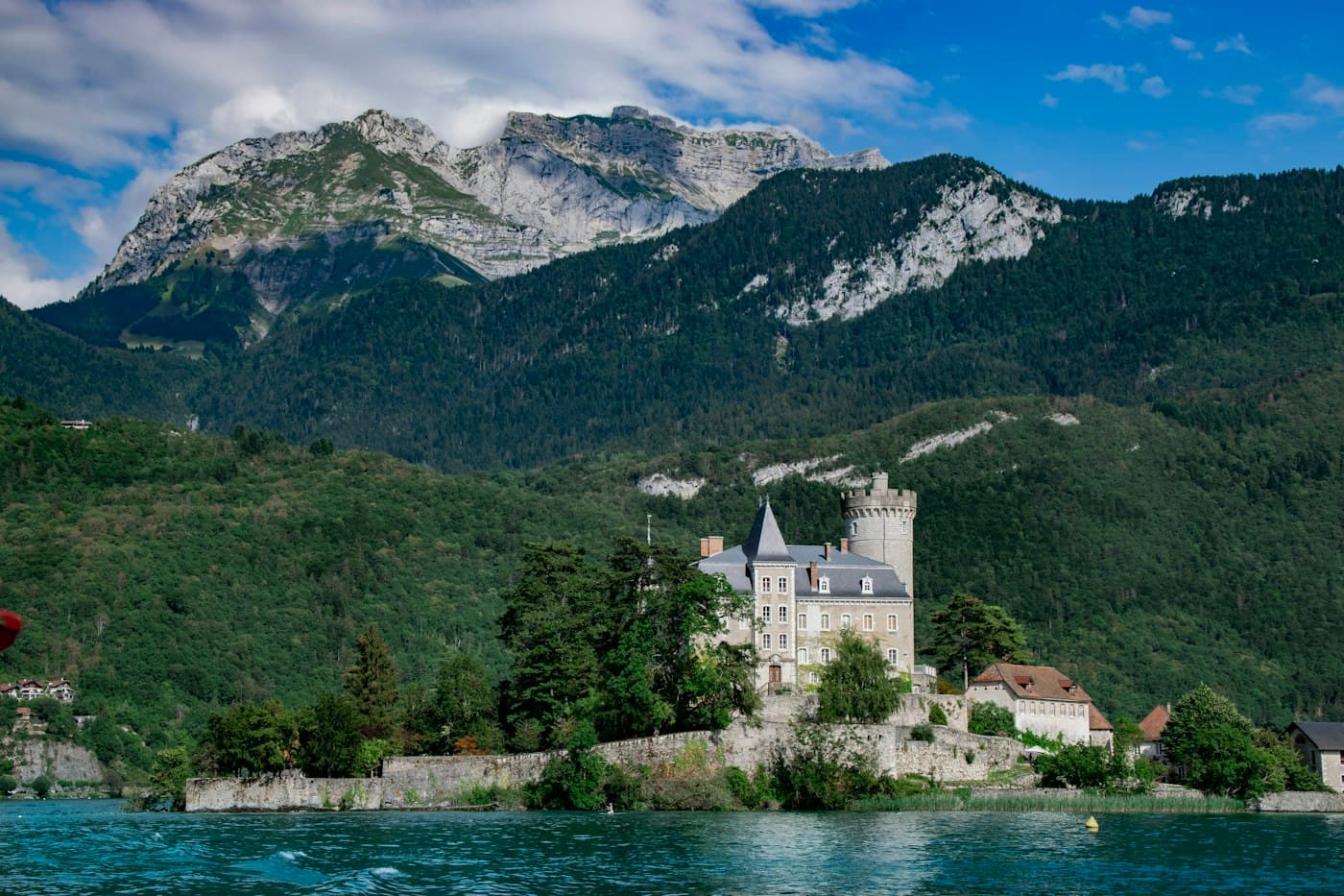 A château with a round tower on the shore of Lake Annecy, below the mountains
