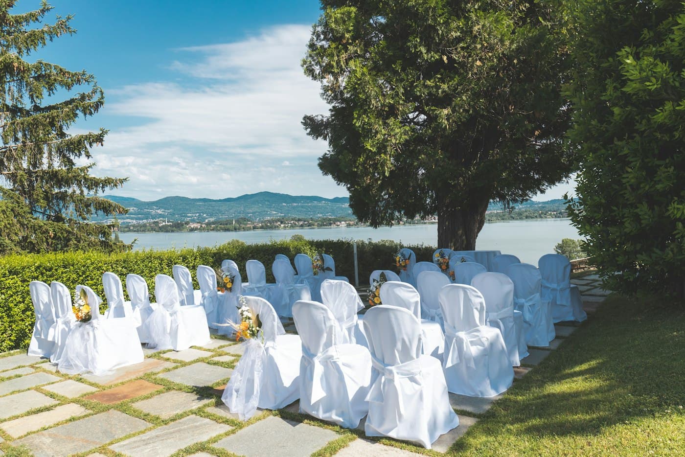 White chairs set for a ceremony on a lawn by a lake