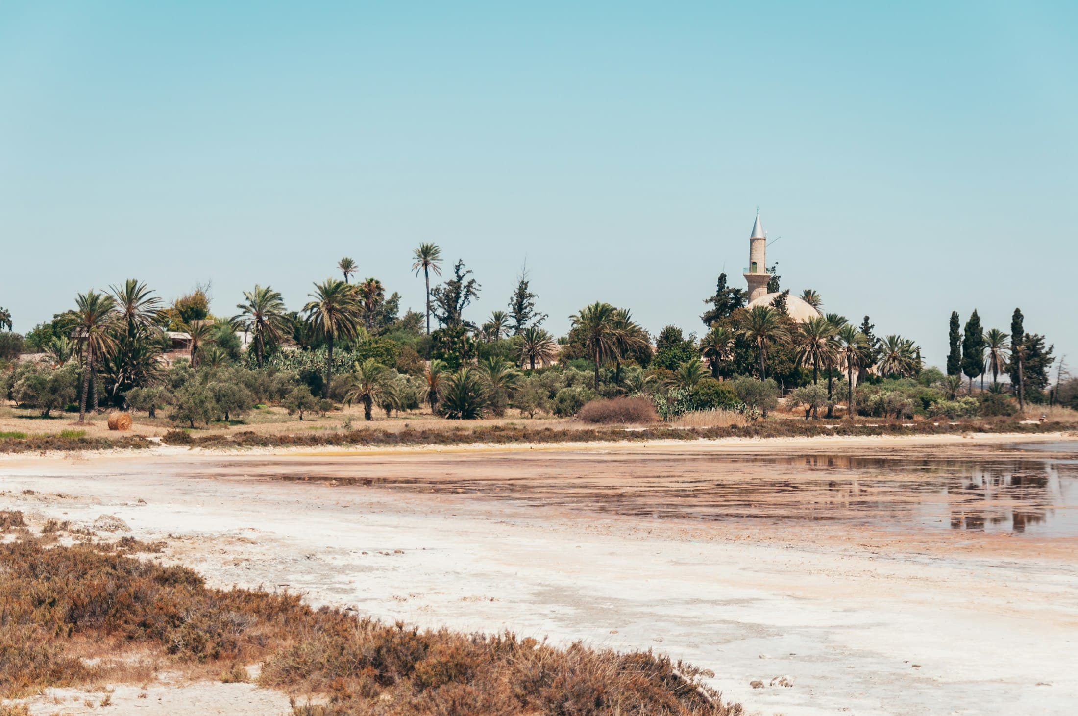 The minaret and dome of Hala Sultan Tekke among palms and cypresses, across the dry white edge of Larnaca’s Salt Lake