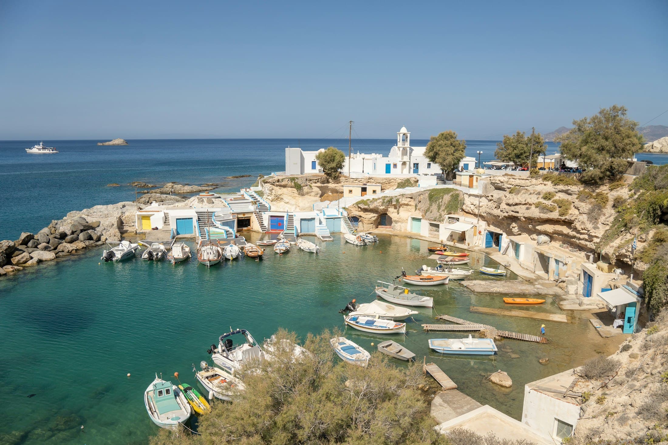 Fischerboote in der Bucht von Mandrakia auf Milos, unter in den Fels gehauenen Bootshäusern und einer weißen Kapelle