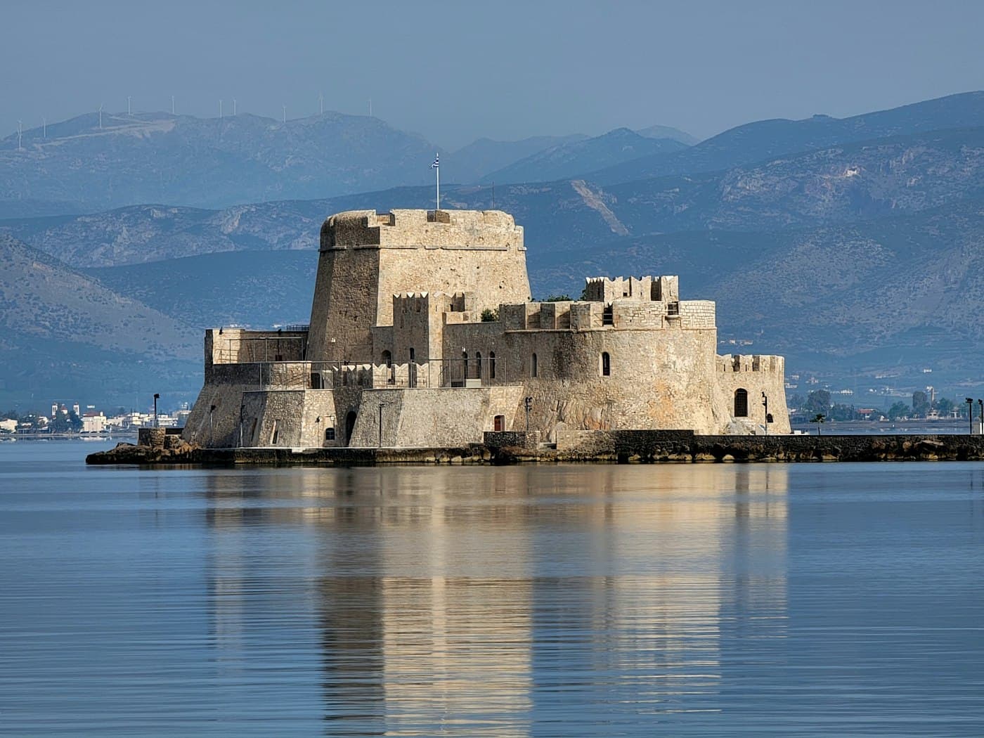 Le Bourtzi, le petit château de la baie de Nauplie, reflété dans l’eau calme, avec les montagnes derrière