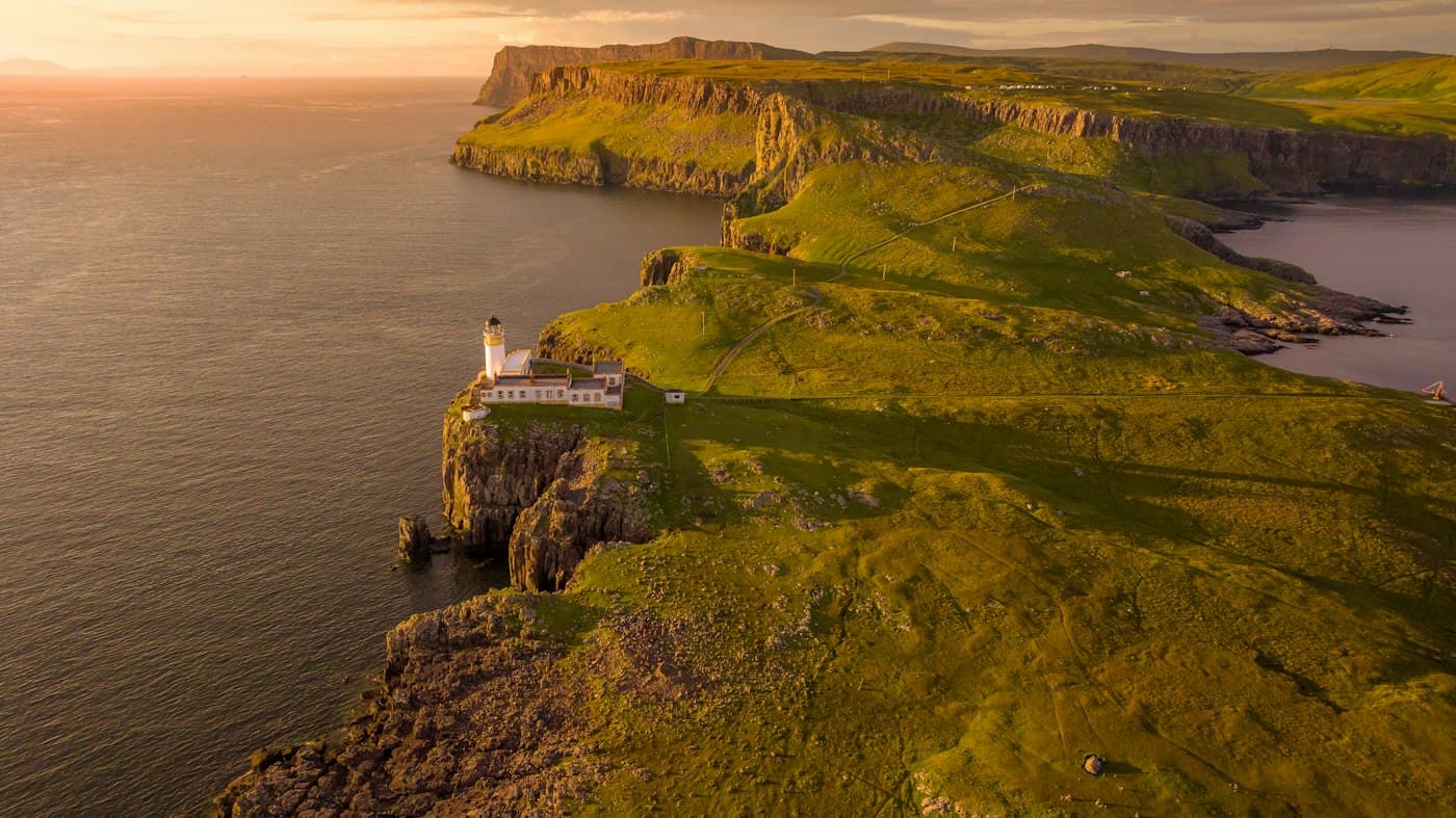 El faro blanco de Neist Point en su promontorio sobre el mar, con los acantilados de la costa oeste de Skye encendidos por la luz baja del atardecer