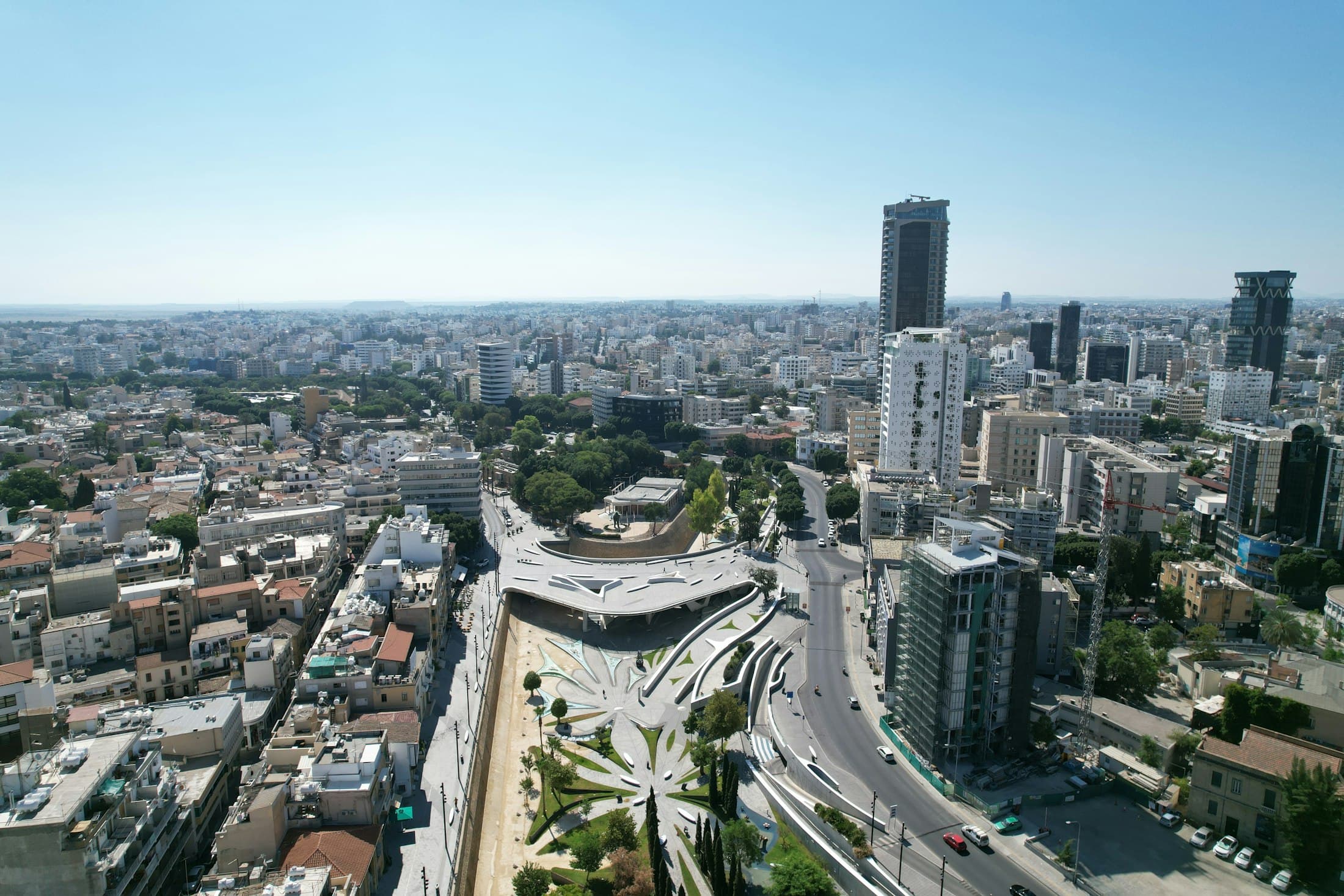 Nicosia from the air on a clear morning: the curving white bridge of Eleftheria Square over the landscaped moat, the old town on the left and the towers of the modern city beyond