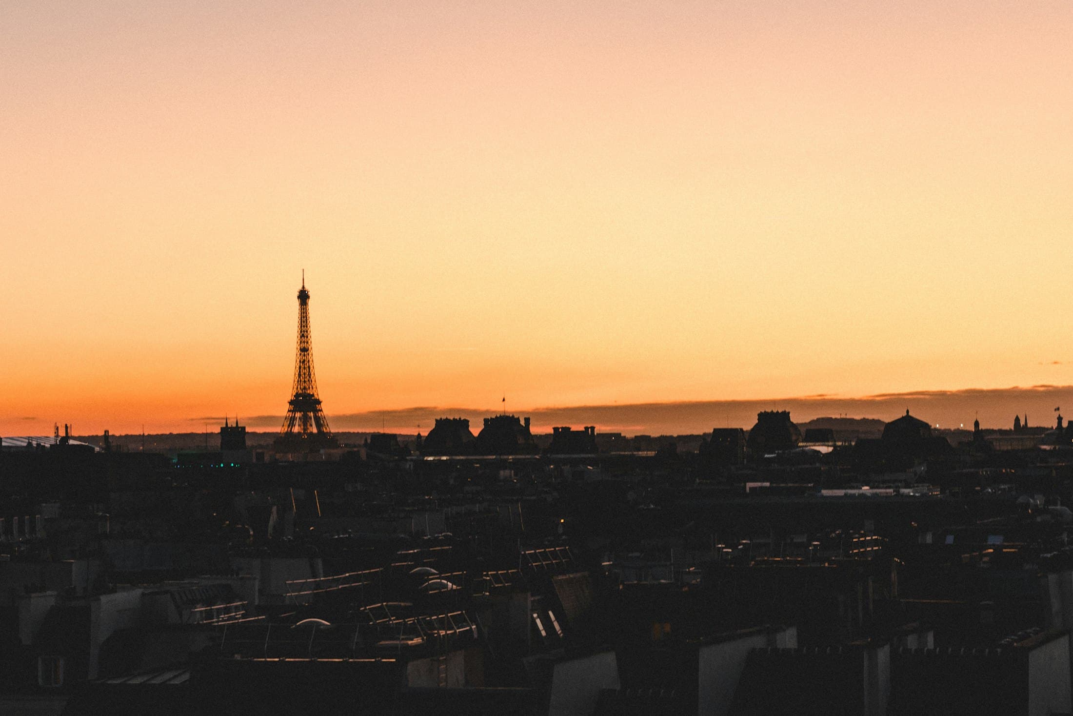 The Eiffel Tower and the rooftops of Paris silhouetted against an orange sunset