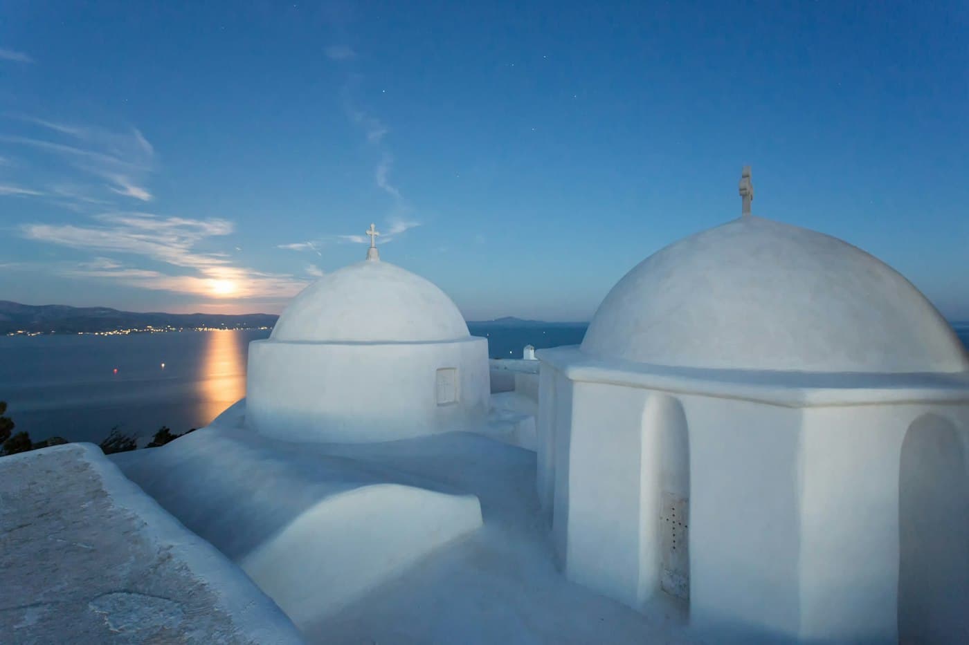 The white domes of a chapel on Paros at dusk, the moon low over the sea